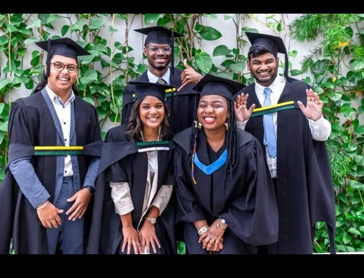 Five graduates smiling together outdoors